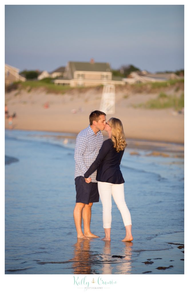 A couple walk through the water and share a kiss on Corporation Beach. 