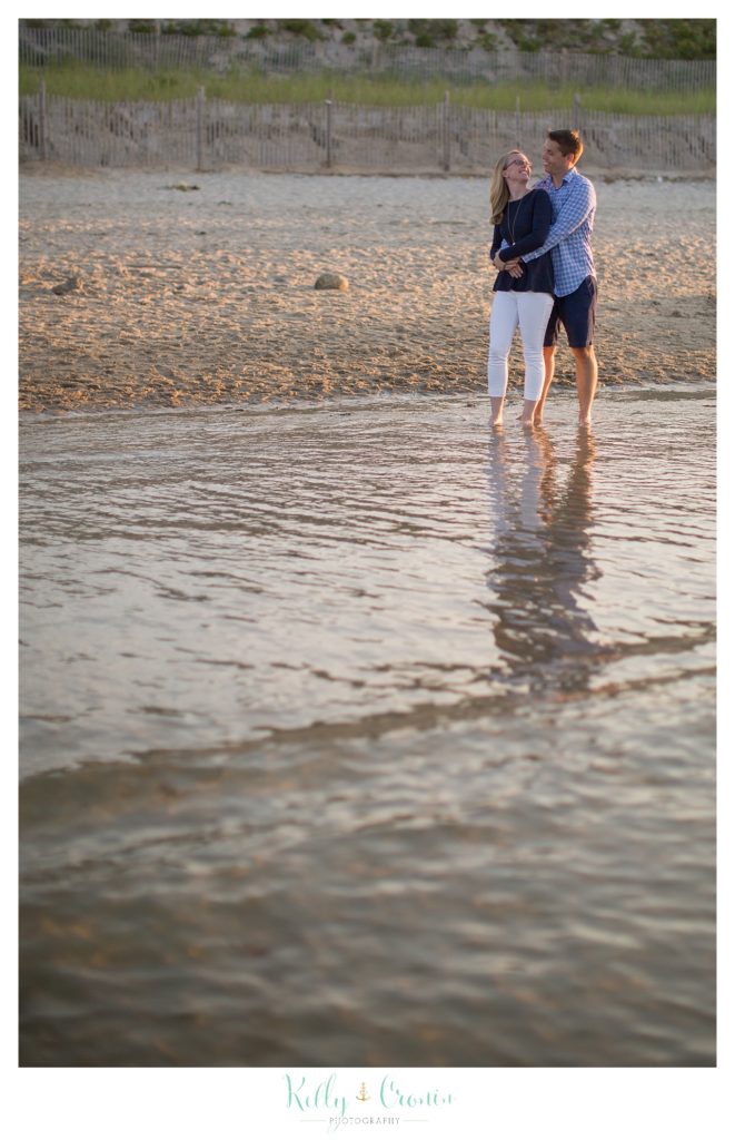 The waves rush up around a couple's feet on Corporation Beach. 