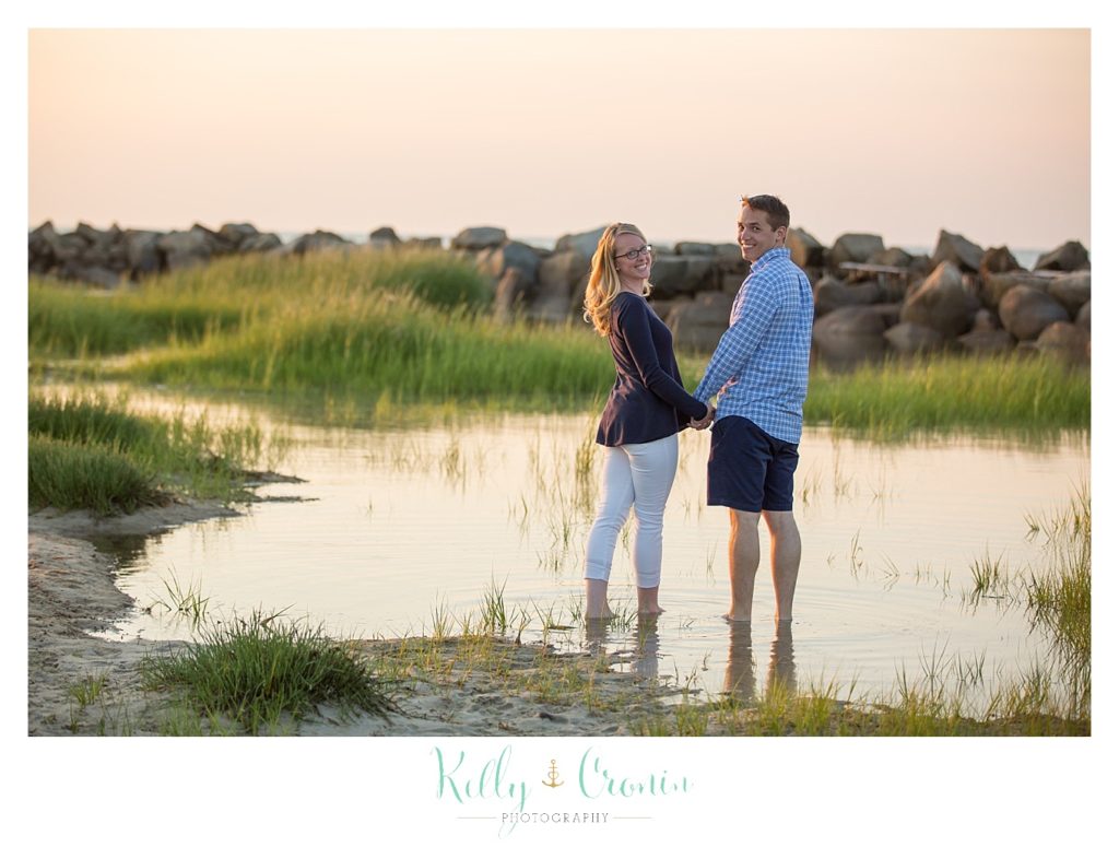 A couple stand in front of the water and hold hands. 
