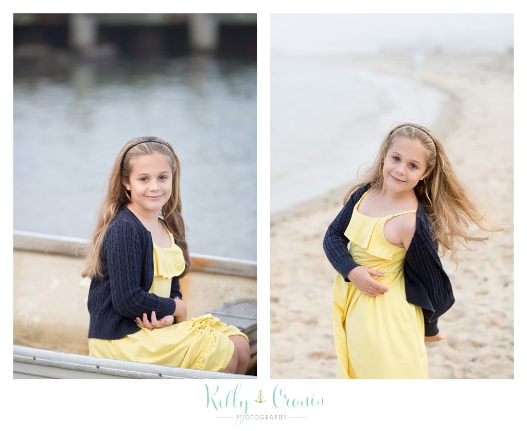 A little girl with long hair and a yellow dress walks on the beach. 