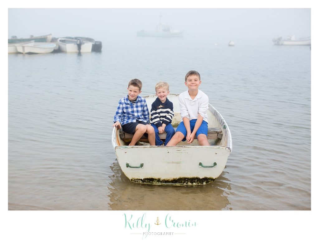 Three young boys crowd into a small wooden boat together. 