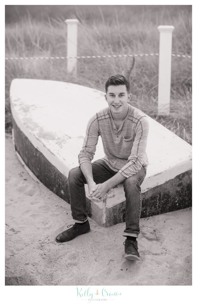 A teenage boy sits on an overturned boat and clasps his hands. 