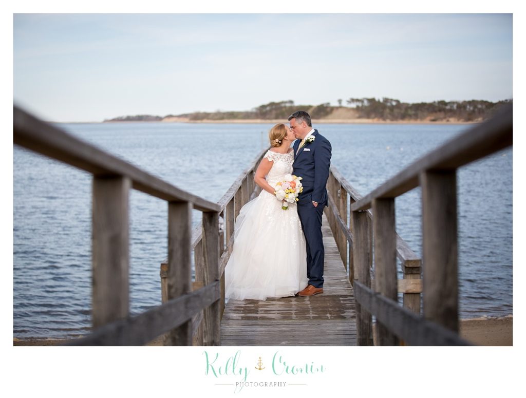 A bride and groom kiss on a pier. 