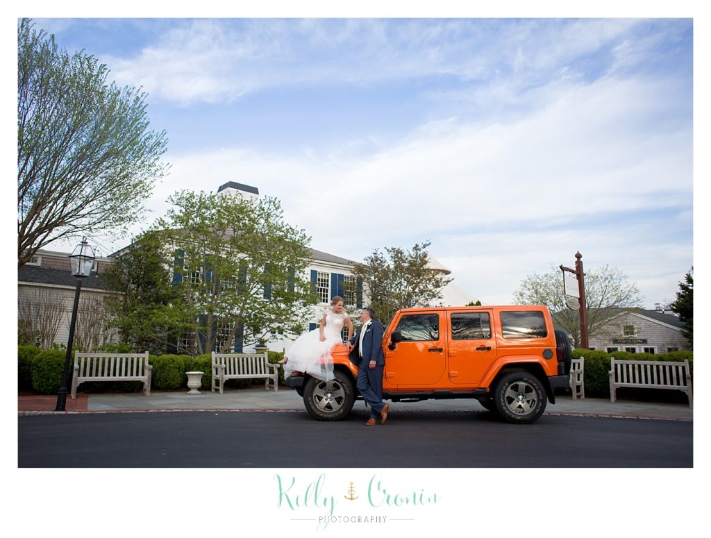 A bride and groom stand in front of an orange jeep. 