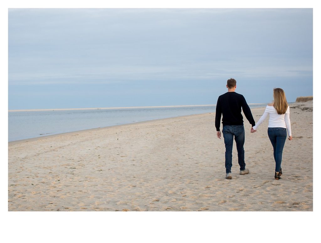 An engaged couple take a walk along the shore. 