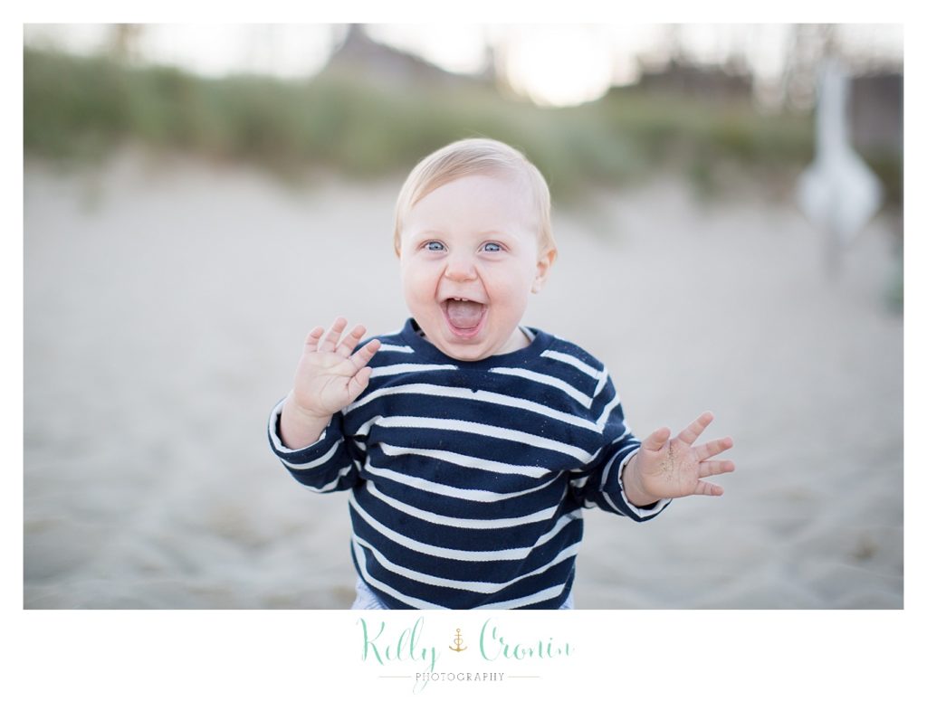 A baby wearing a navy striped shirt laughs as he walks. 