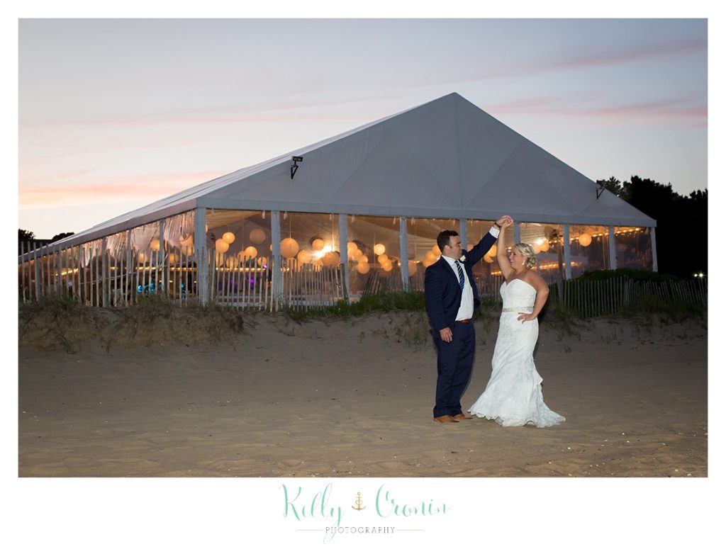 A wedding tent is lit with the bride and groom standing in front. 