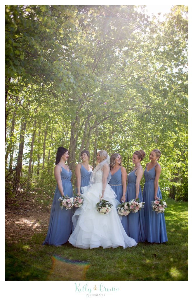 A bride and her bridal party stand in the trees. 