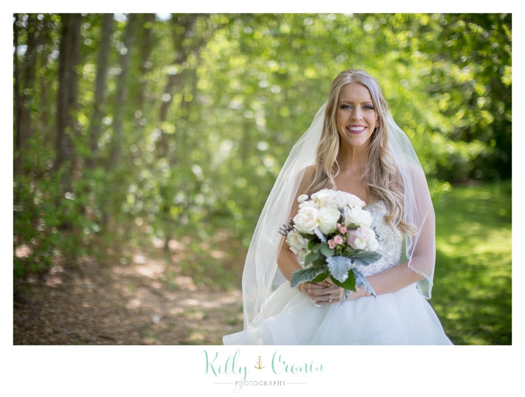 A bride holds her bouquet in the woods. 