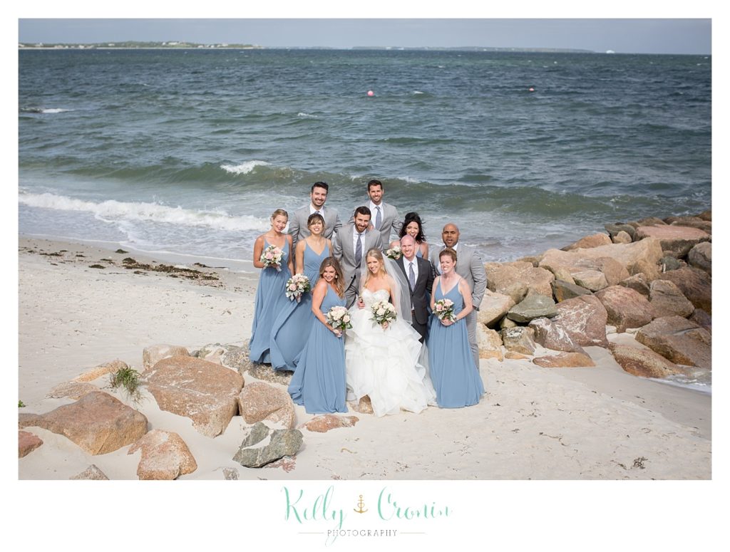 A bridal party stands on the beach together. 