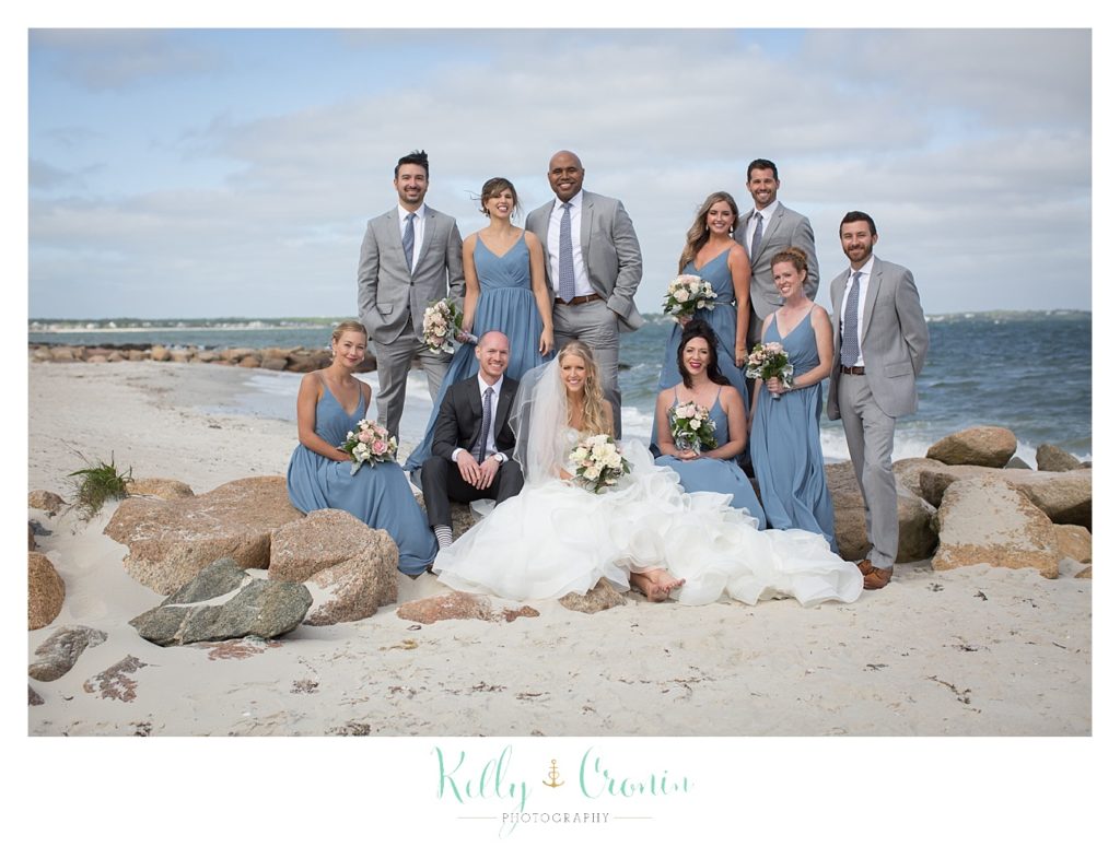 A wedding party stands on the beach together. 