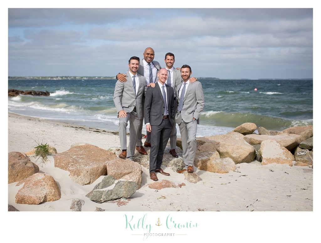 A groom stands on the beach with his groomsmen. 