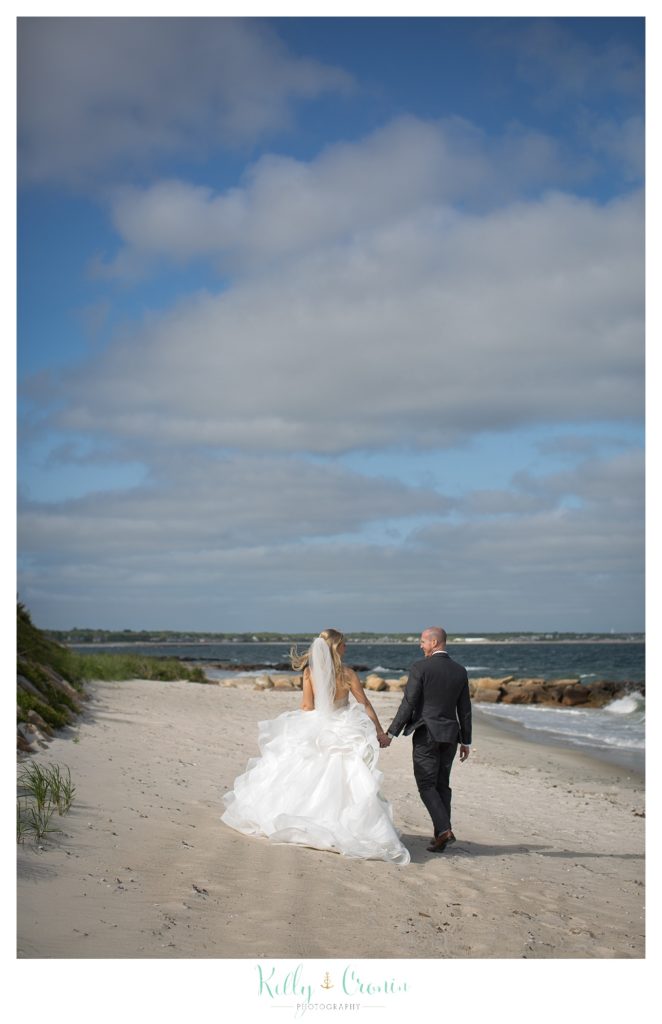 A bride and groom walk along the beach together. 