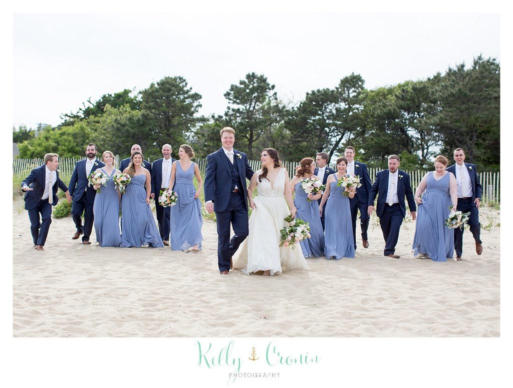 A bride and groom laugh while standing in front of their bridal party. 