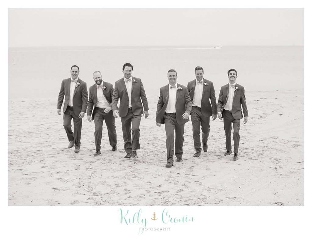 A groom and his groomsmen walk along the beach together. 