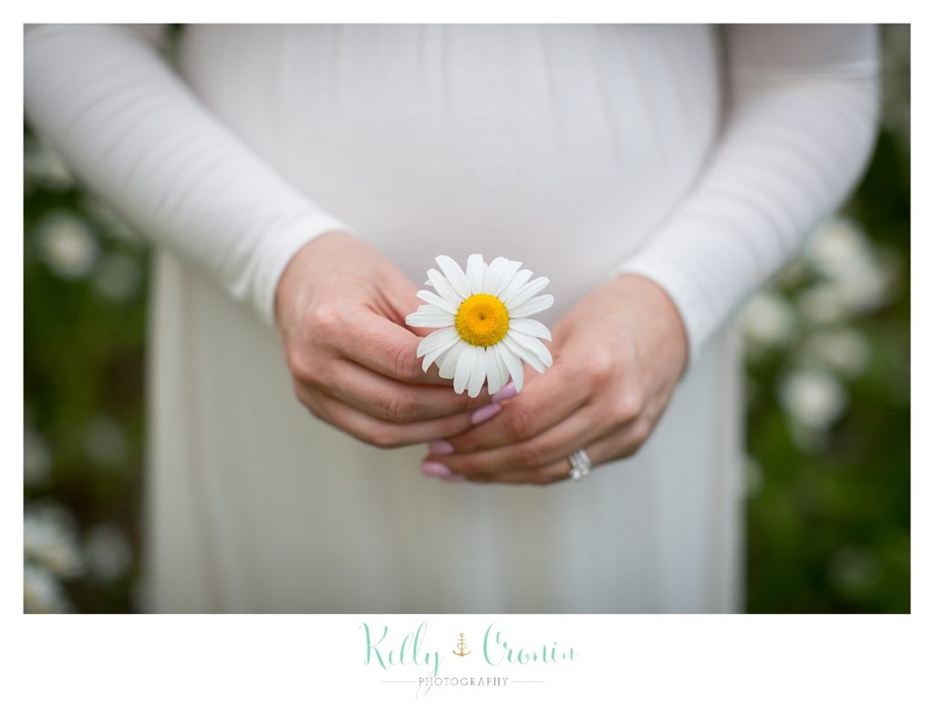 A pregnant woman holds a wildflower in front of her tummy. 