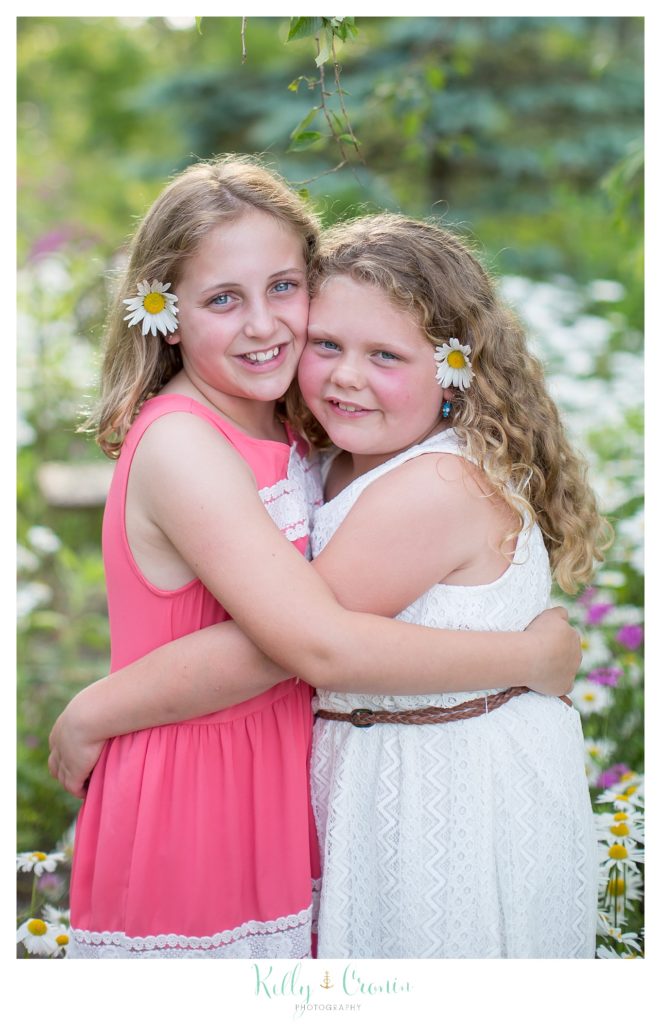 Two sisters hug as they stand among some wildflowers. 
