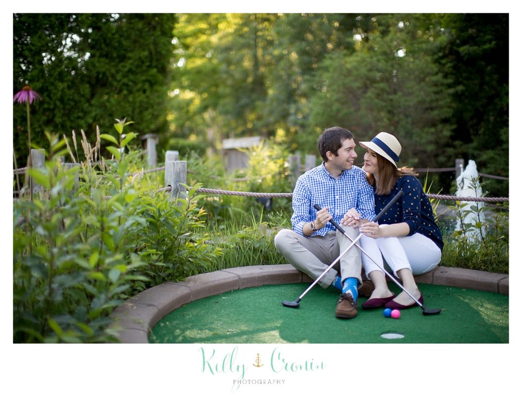 A couple sit at a hole during mini golf. 