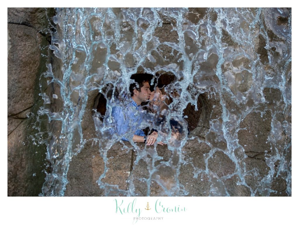 A couple kiss behind a waterfalls. 