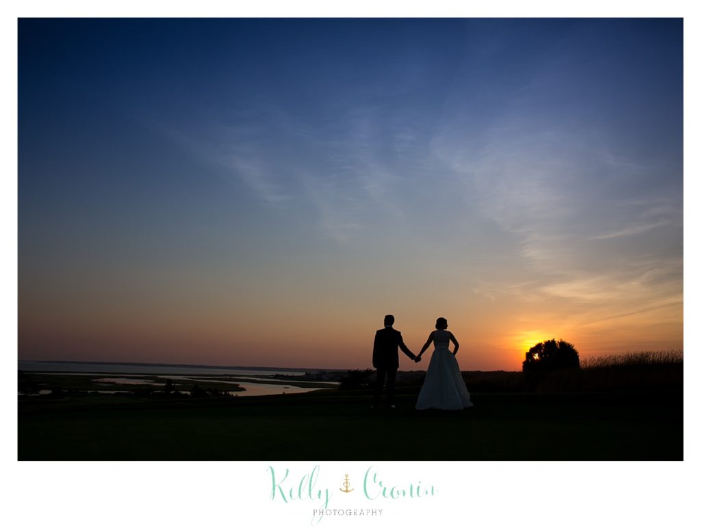A bride and groom stand in front of a sunset for their wedding. 