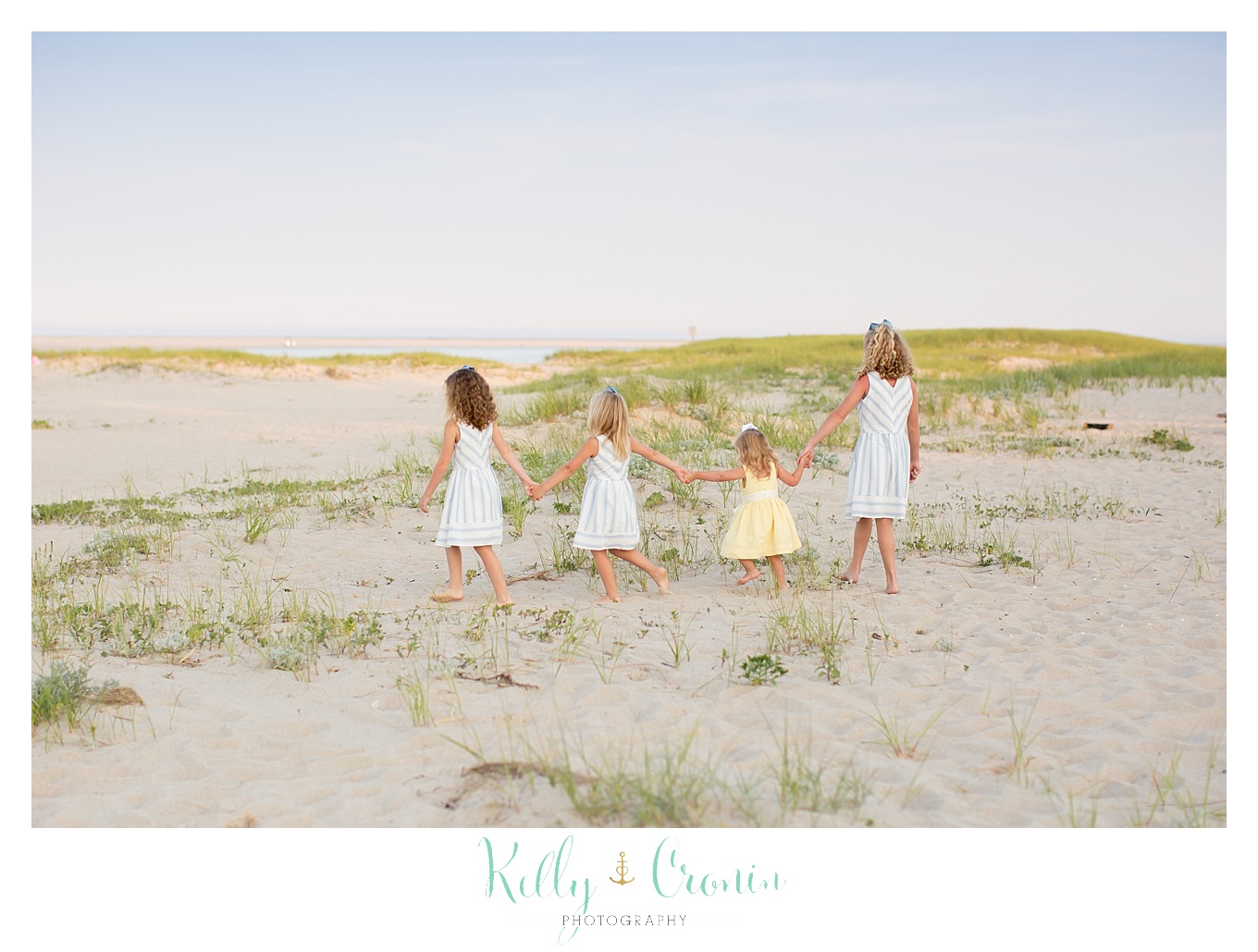 Four young girls walk along the beach, holding hands.