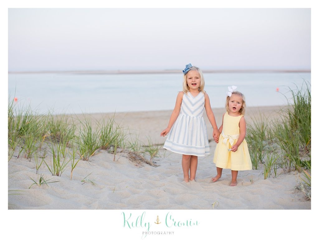 Two young sisters stand in the sand during their seaside photography session. 