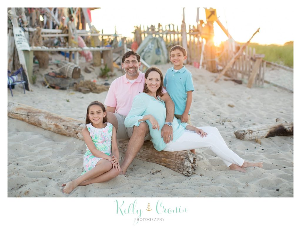 A family sits in the sand on the beach for a family photo. 