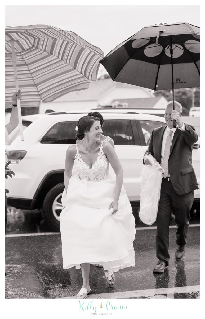 A bride walks under an umbrella towards her wedding venue. 