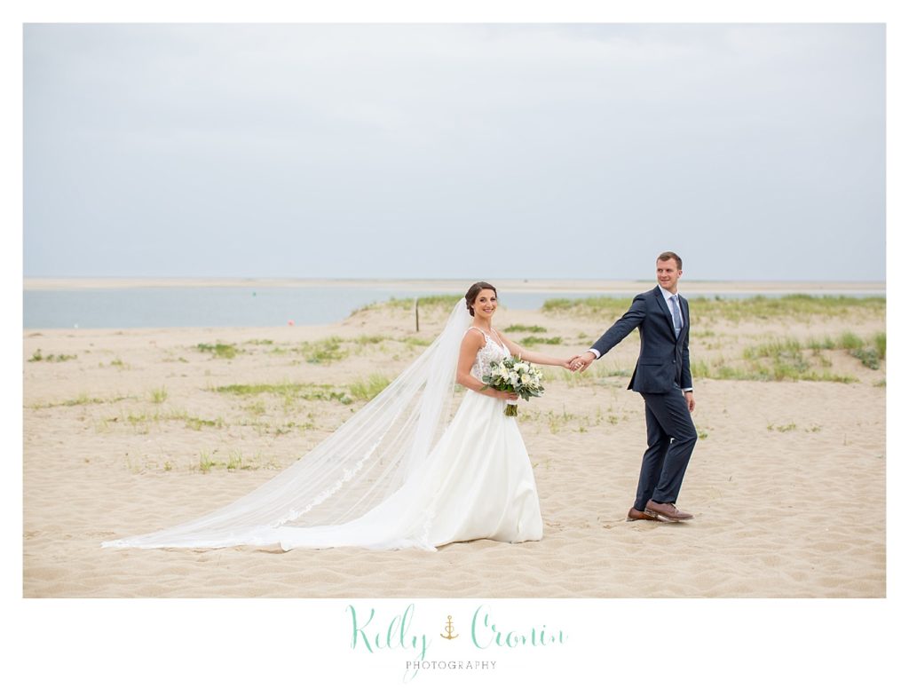 A groom leads his bride on a walk along the beach. 