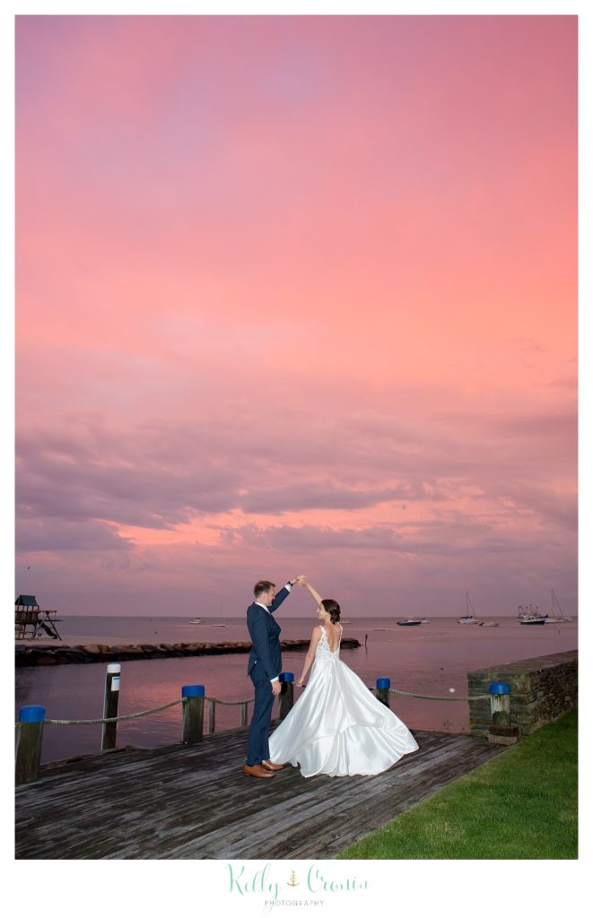 A bride and groom dance under a pink sunset. 