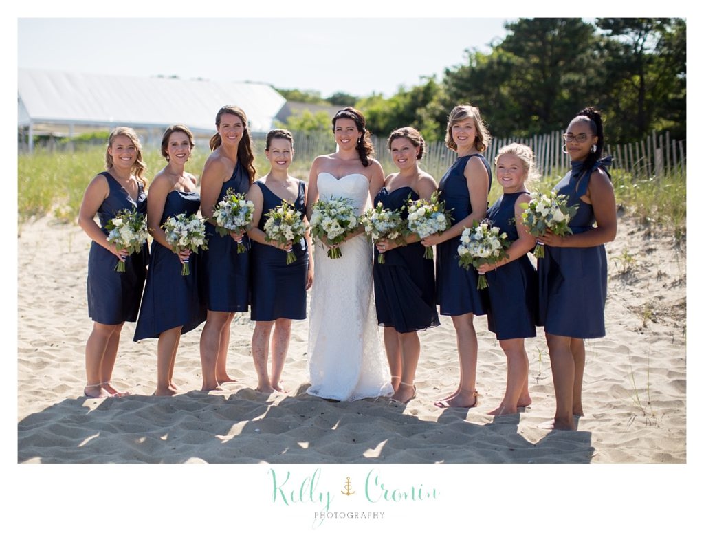 A wedding party stands in the sand on the beach.