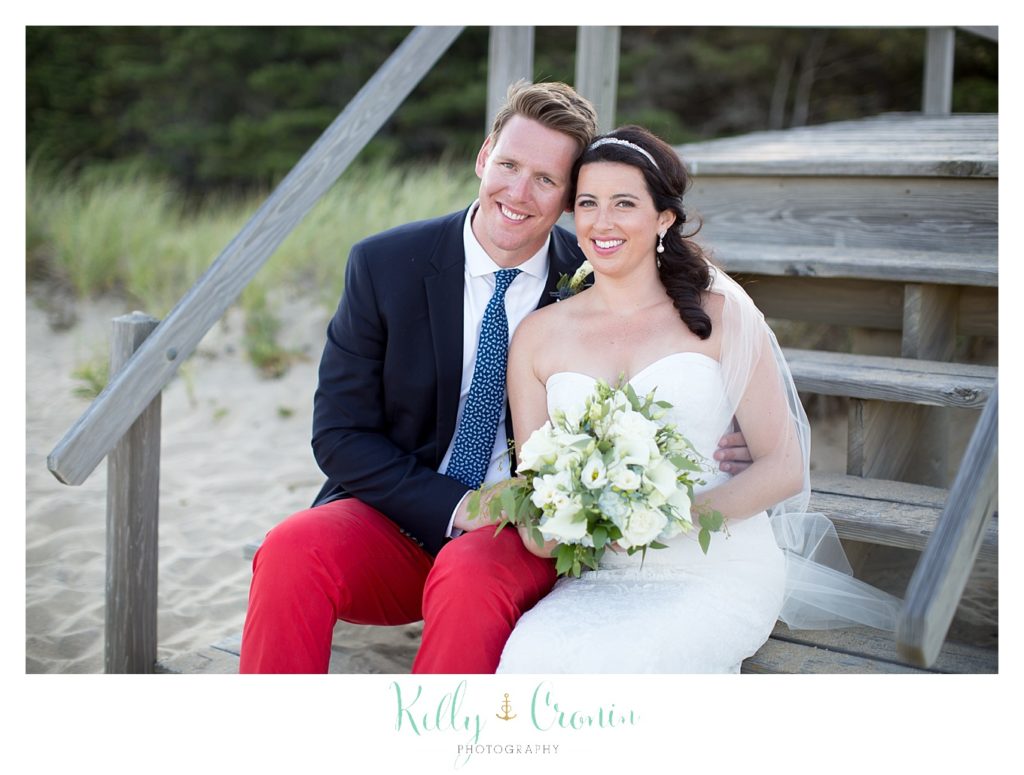A groom in red pants sits next to his bride on some stairs.