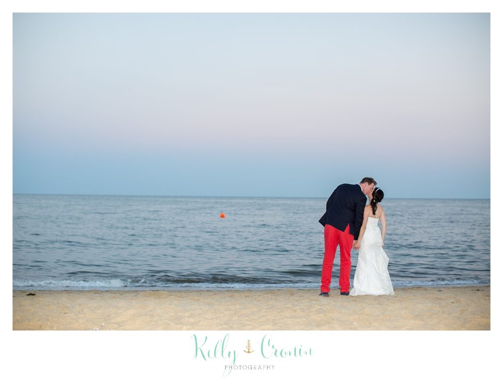 A bride and groom kiss in front of the ocean.