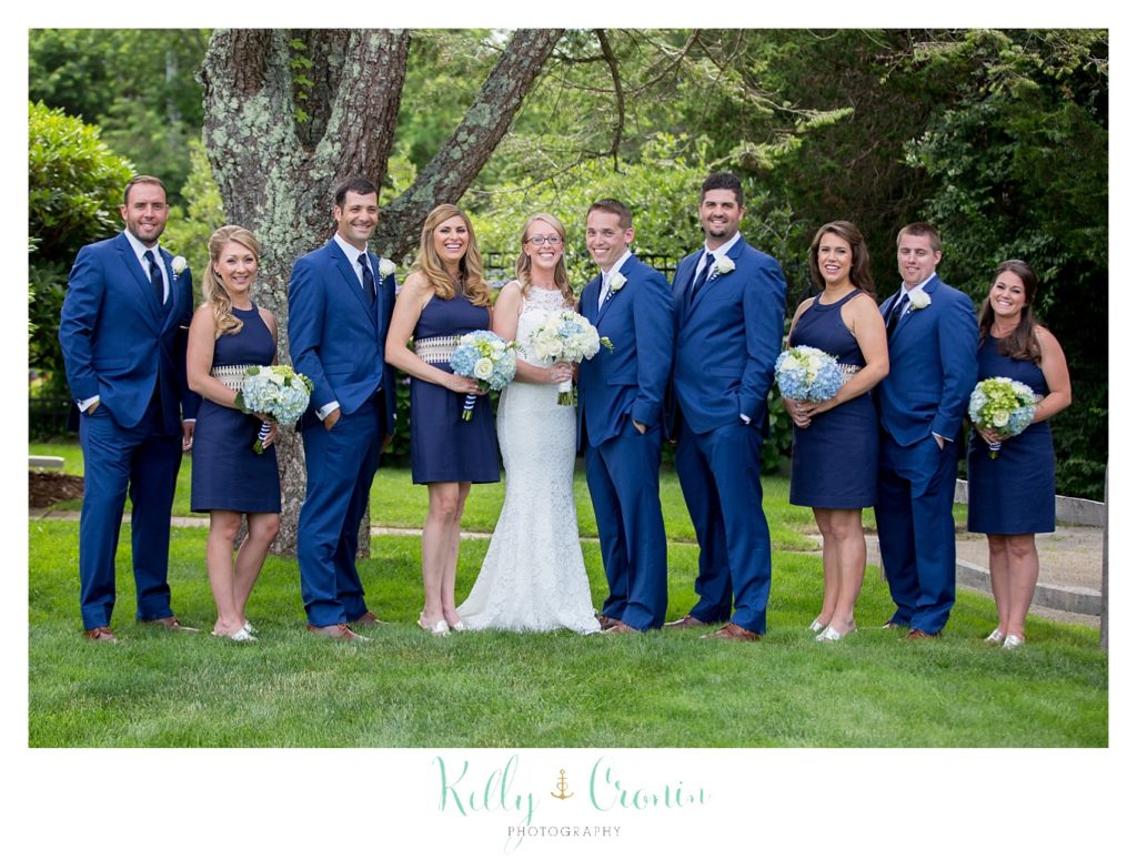 A wedding party poses in front of some large trees. 