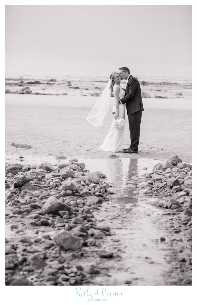 A groom kisses his new bride on the beach. 