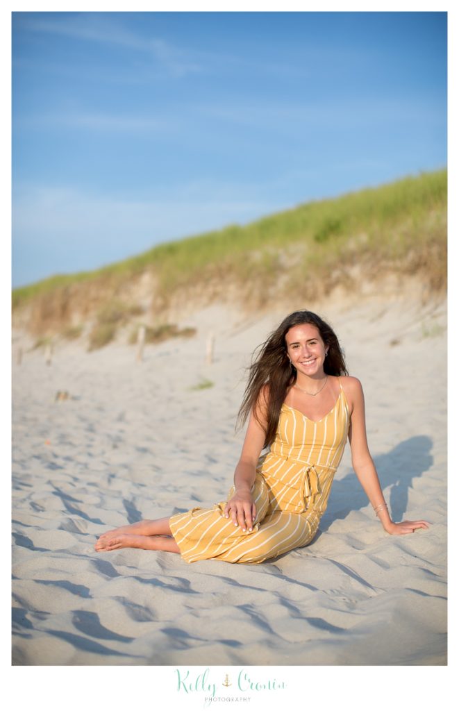 A young woman wearing a yellow dress sits on the beach. 