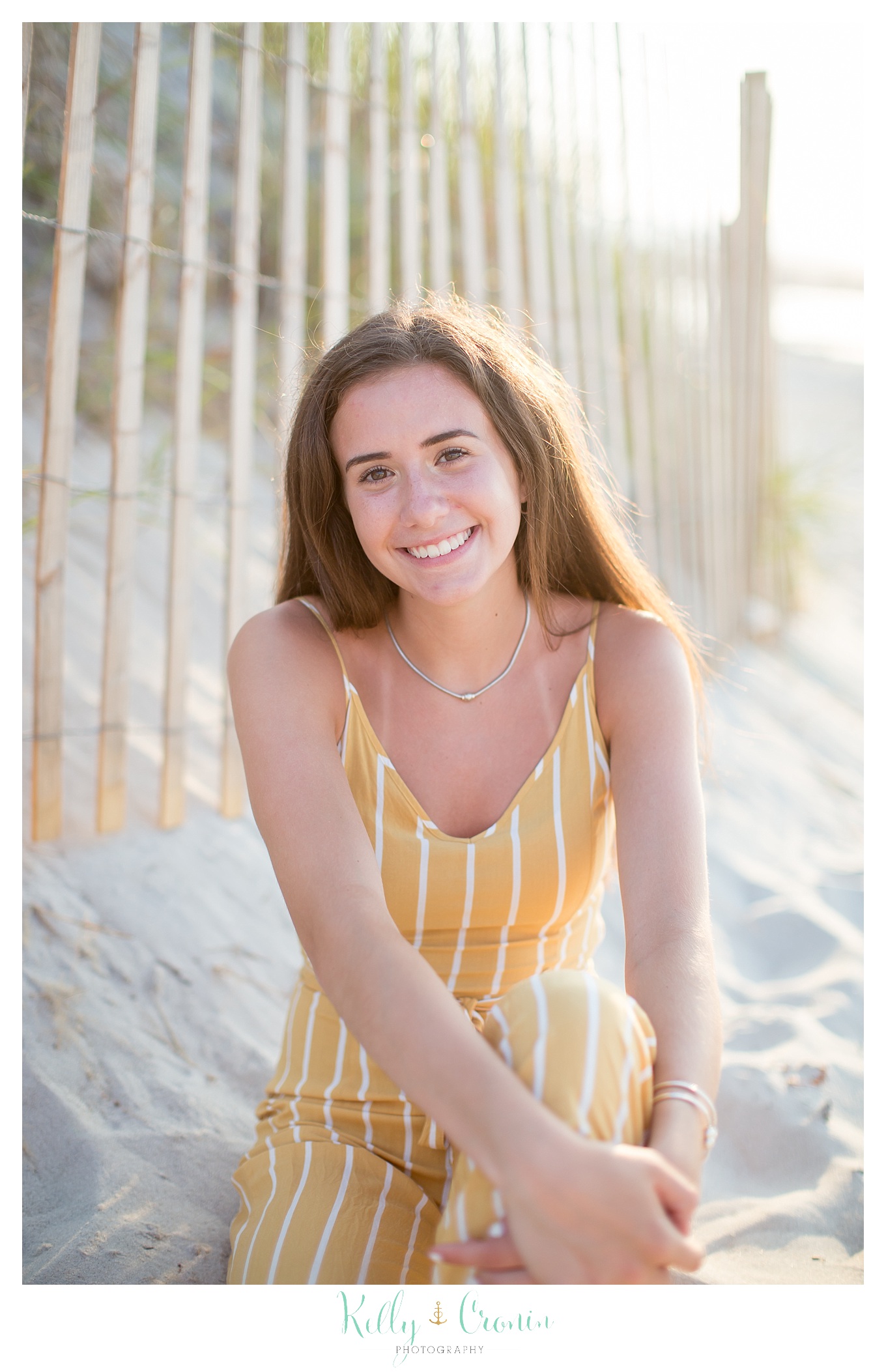 A young lady wearing yellow smiles for her senior portraits.
