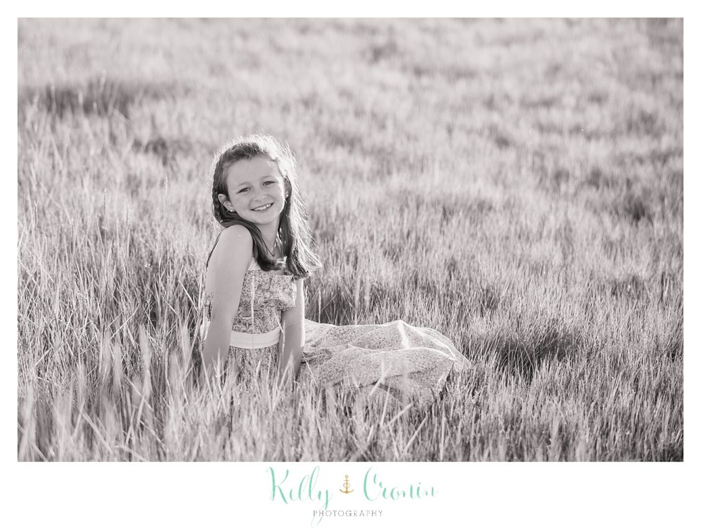 A little girl sits in a field of tall grass, almost blending in. 