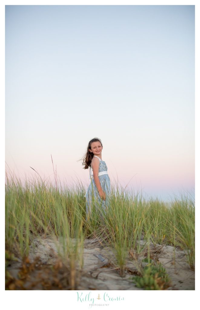 A young girl looks over her shoulder as she walks through tall grass. 