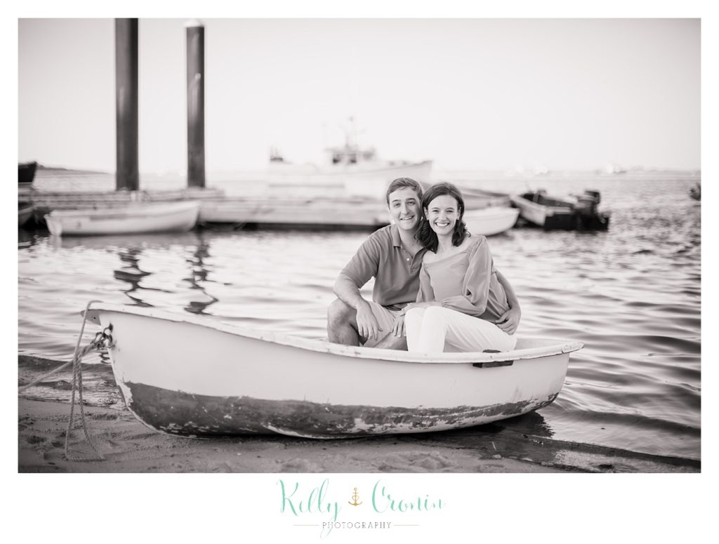 An engaged couple sit on a small wooden boat together. 