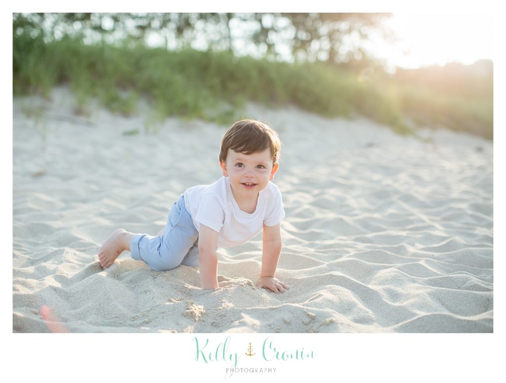 A toddler crawl in the sand on the beach. 