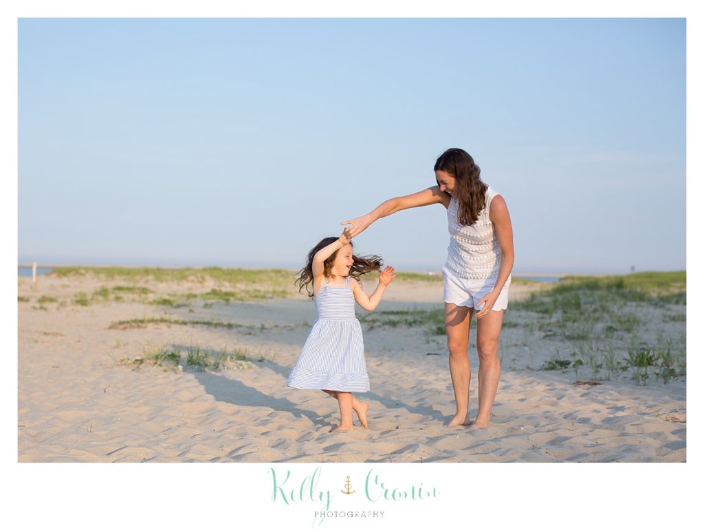 A woman dances with her young daughter on the beach. 