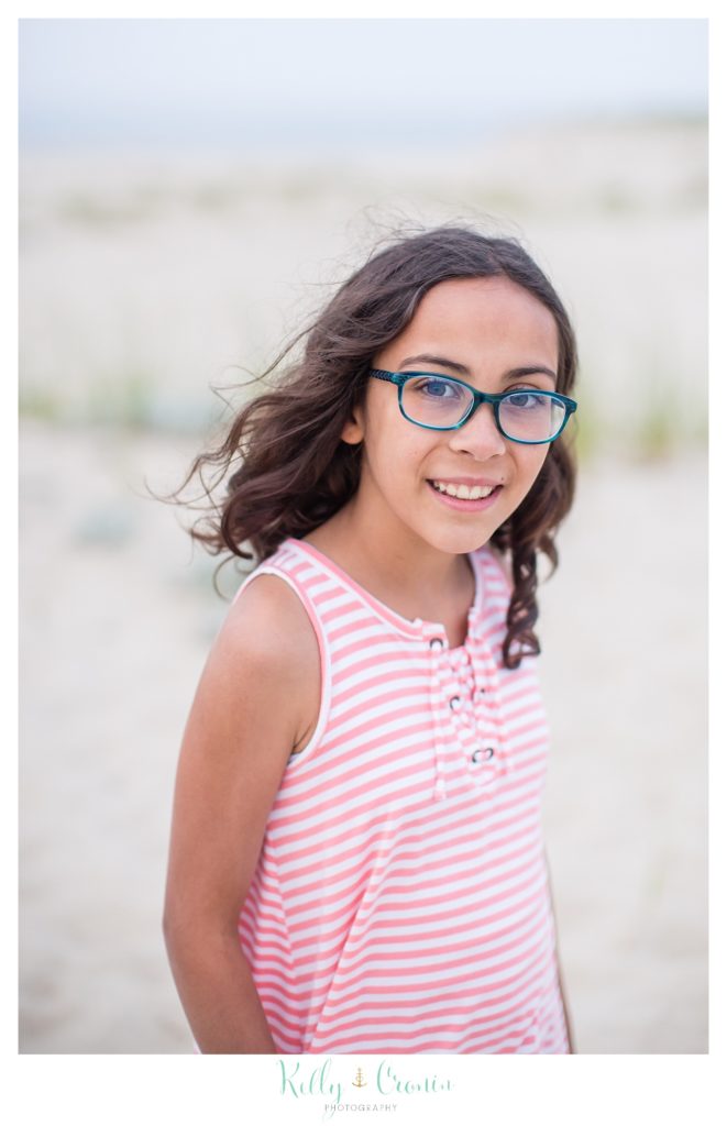 A girl wearing glasses and a pink shirt smiles. 