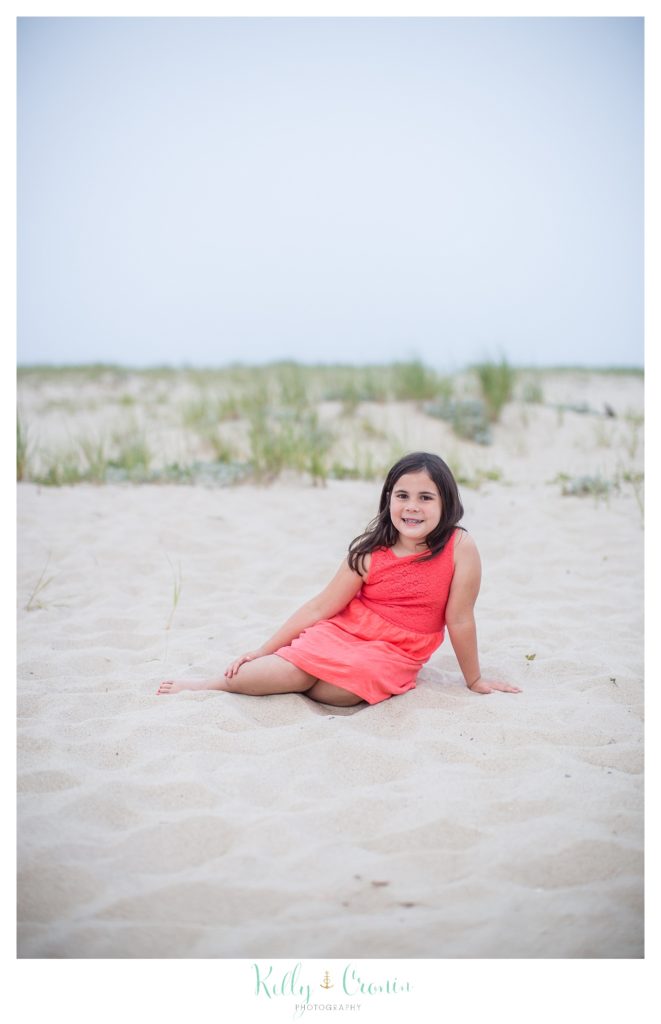 A girl sits in the sand on a Cape Cod beach. 