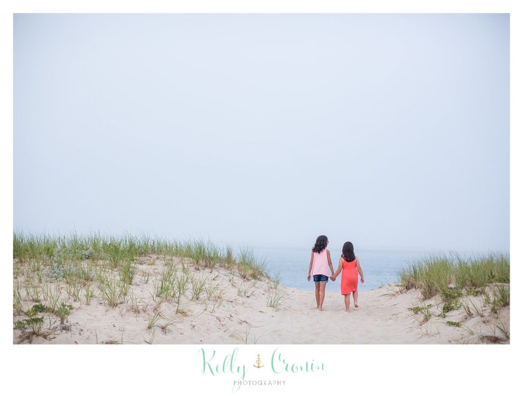 Two girls hold hands and take a walk on the beach. 