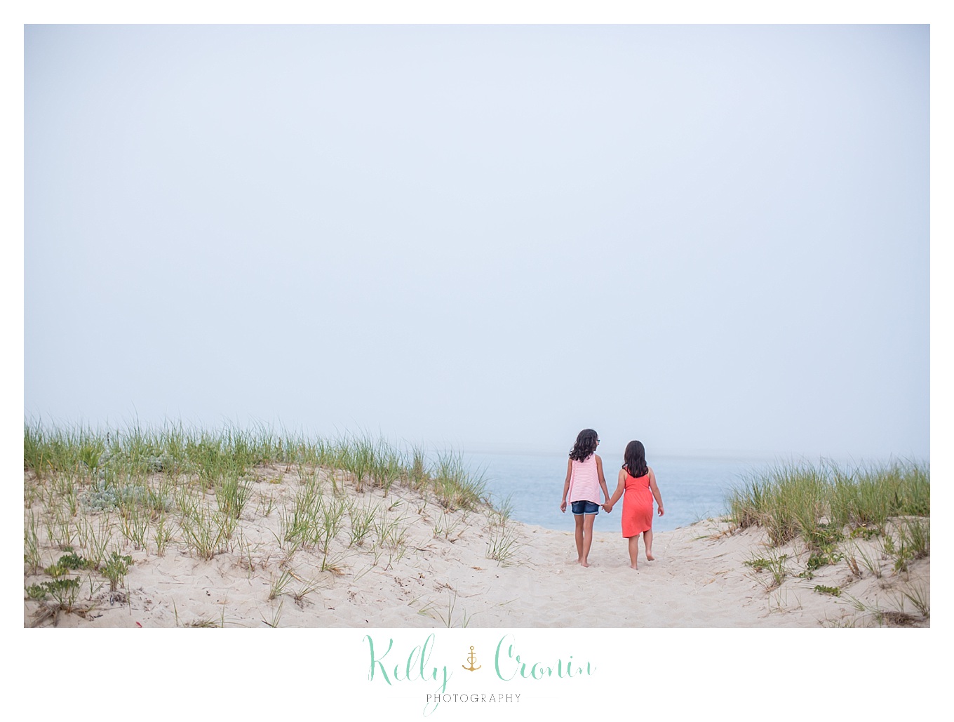 Two girls hold hands and take a walk on the beach.
