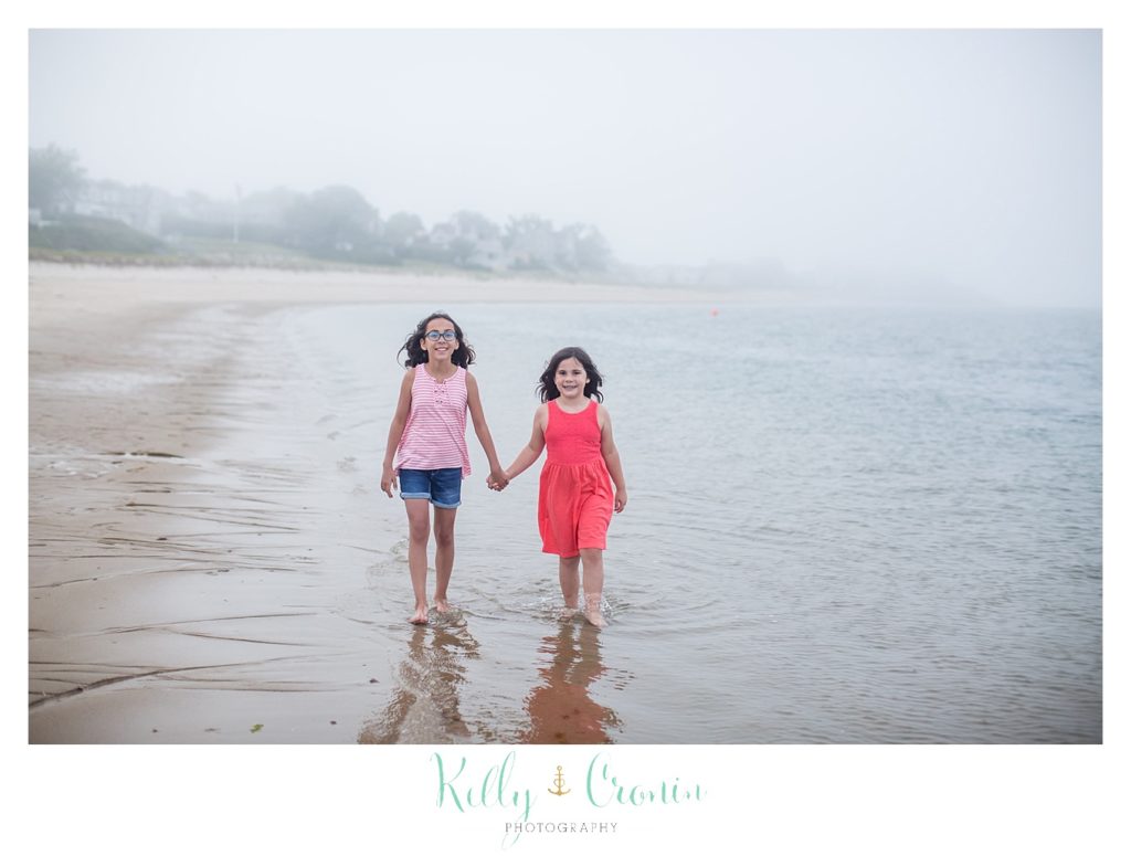 Two sisters walk in the water on the beach. 