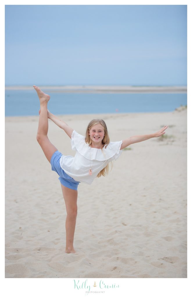 A girl does a gymnastic move on the beach. 