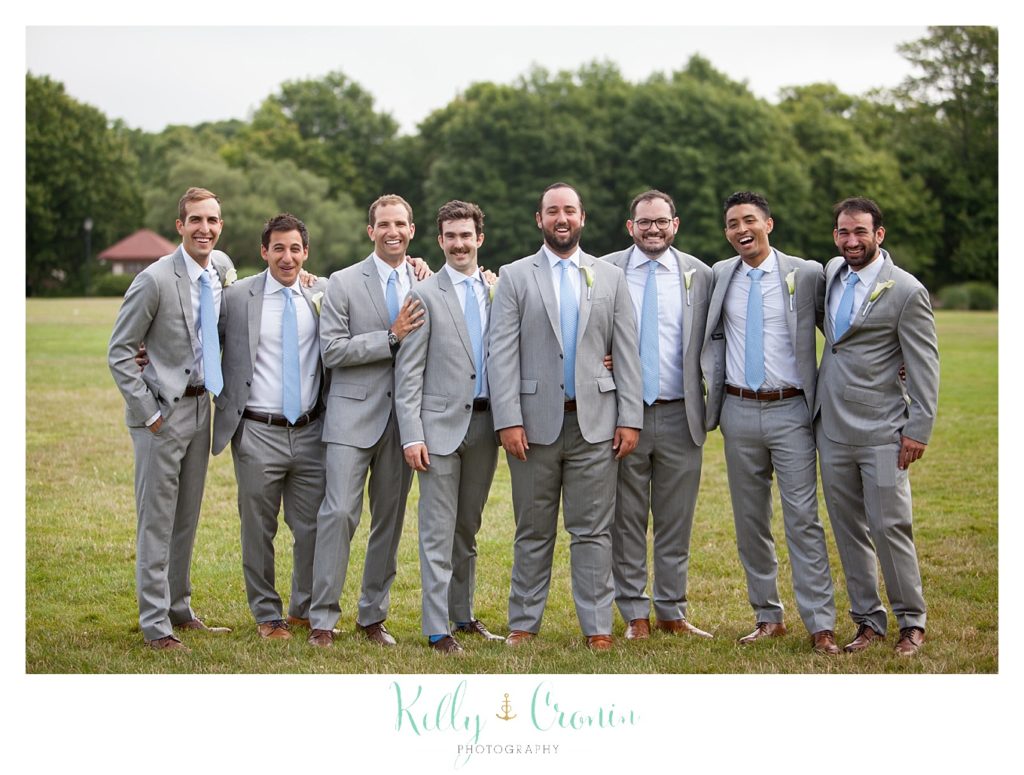 A groom stands with his groomsmen in the grass. 