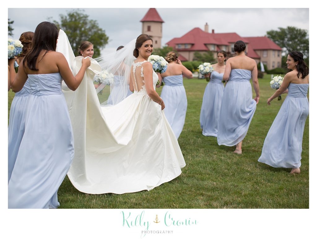 A bridesmaid holds the bride's train as they walk to the Ocean Edge Wedding. 